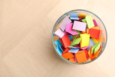 Photo of Jar with colorful pieces of paper on wooden table, top view. Space for text
