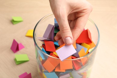 Photo of Woman taking paper with message out of jar at wooden table, closeup