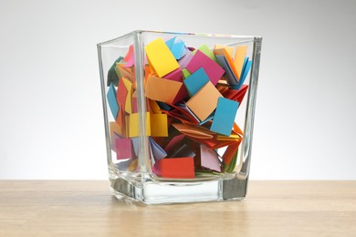 Photo of Jar with colorful pieces of paper on wooden table against light background
