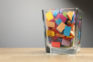 Photo of Jar with colorful pieces of paper on wooden table against grey background. Space for text