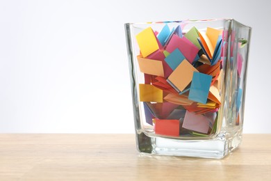 Photo of Jar with colorful pieces of paper on wooden table against light background. Space for text