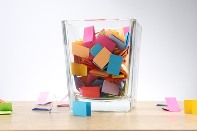 Photo of Jar with colorful pieces of paper on wooden table against light background