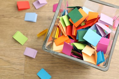 Photo of Jar with colorful pieces of paper on wooden table, top view