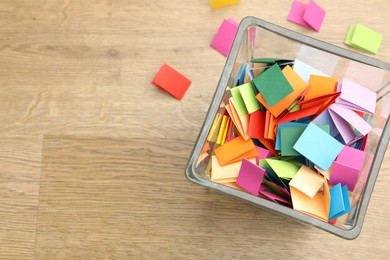 Photo of Jar with colorful pieces of paper on wooden table, top view. Space for text
