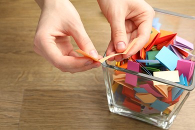 Photo of Woman taking paper with message out of jar at wooden table, closeup