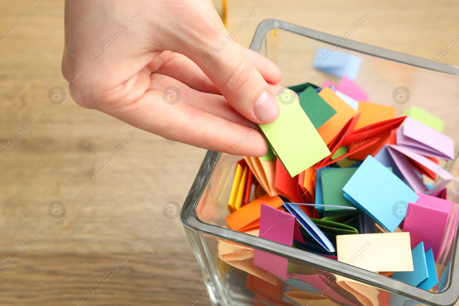 Woman taking paper with message out of jar at wooden table, closeup Photo of Woman taking paper with message out of jar at wooden table, closeup