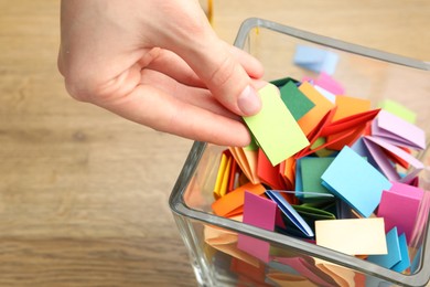 Photo of Woman taking paper with message out of jar at wooden table, closeup
