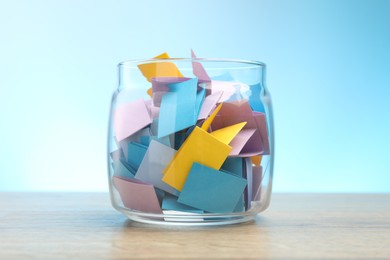 Photo of Jar with colorful pieces of paper on wooden table against light blue background