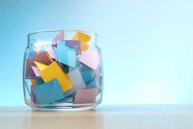 Photo of Jar with colorful pieces of paper on wooden table against light blue background. Space for text