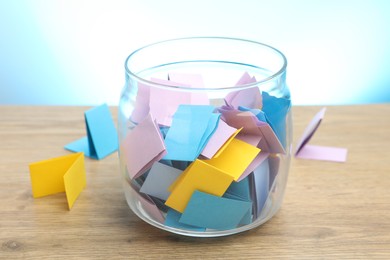 Photo of Jar with colorful pieces of paper on wooden table against light blue background