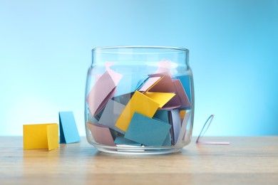 Photo of Jar with colorful pieces of paper on wooden table against light blue background