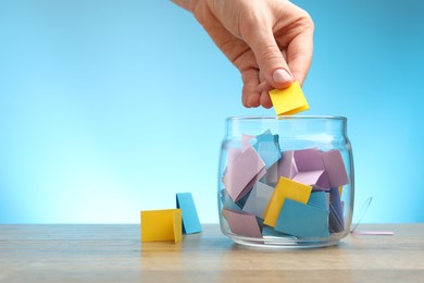 Photo of Woman taking paper with message out of jar at wooden table, closeup. Space for text