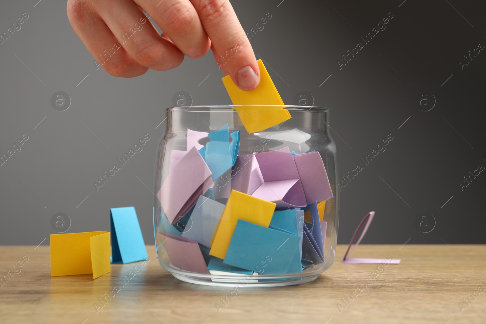 Photo of Woman taking paper with message out of jar at wooden table, closeup