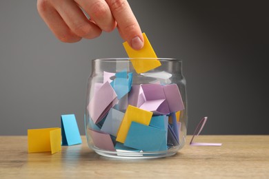 Photo of Woman taking paper with message out of jar at wooden table, closeup