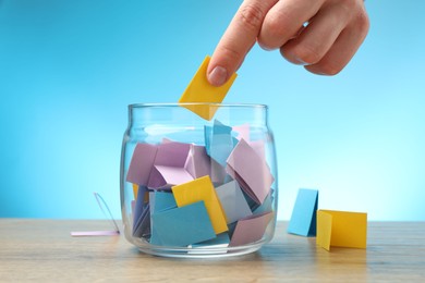 Photo of Woman taking paper with message out of jar at wooden table, closeup