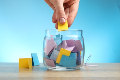 Photo of Woman taking paper with message out of jar at wooden table, closeup