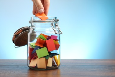 Photo of Woman taking paper with message out of jar at wooden table, closeup. Space for text