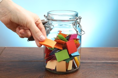 Photo of Woman taking paper with message out of jar at wooden table, closeup
