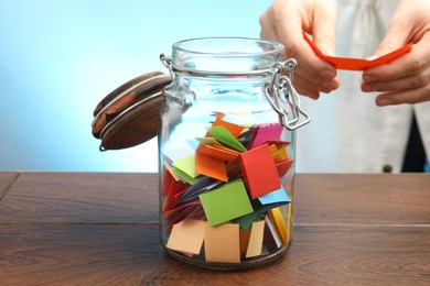 Photo of Woman taking paper with message out of jar at wooden table, closeup