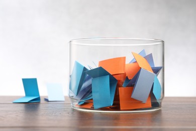 Photo of Jar with colorful pieces of paper on wooden table against light background