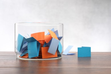 Photo of Jar with colorful pieces of paper on wooden table against light background