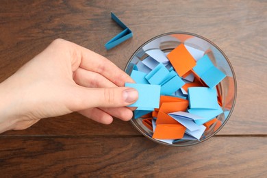 Photo of Woman taking paper with message out of jar at wooden table, top view