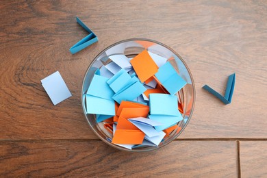 Photo of Jar with colorful pieces of paper on wooden table, top view