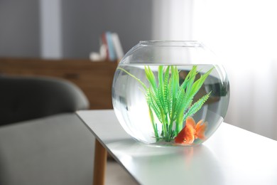 Photo of Beautiful goldfish in round aquarium on white table indoors. Space for text