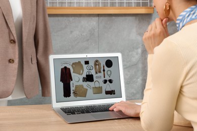 Photo of Professional stylist with picture of outfit on laptop at desk indoors