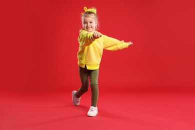 Photo of Cute little girl dancing on red background