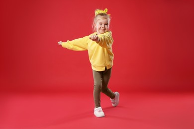 Photo of Cute little girl dancing on red background