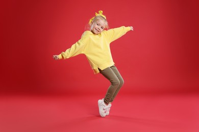 Photo of Cute little girl dancing on red background
