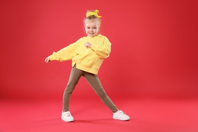 Photo of Cute little girl dancing on red background