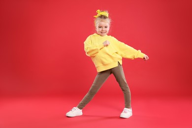 Photo of Cute little girl dancing on red background