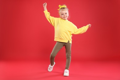 Photo of Cute little girl dancing on red background