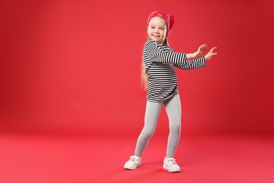 Photo of Cute little girl dancing on red background, space for text