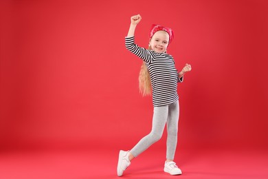 Photo of Cute little girl dancing on red background, space for text