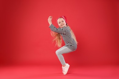 Photo of Cute little girl dancing on red background