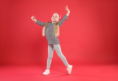 Photo of Cute little girl dancing on red background