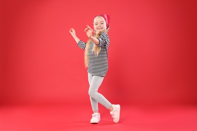 Photo of Cute little girl dancing on red background