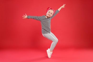 Photo of Cute little girl dancing on red background
