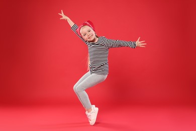 Photo of Cute little girl dancing on red background