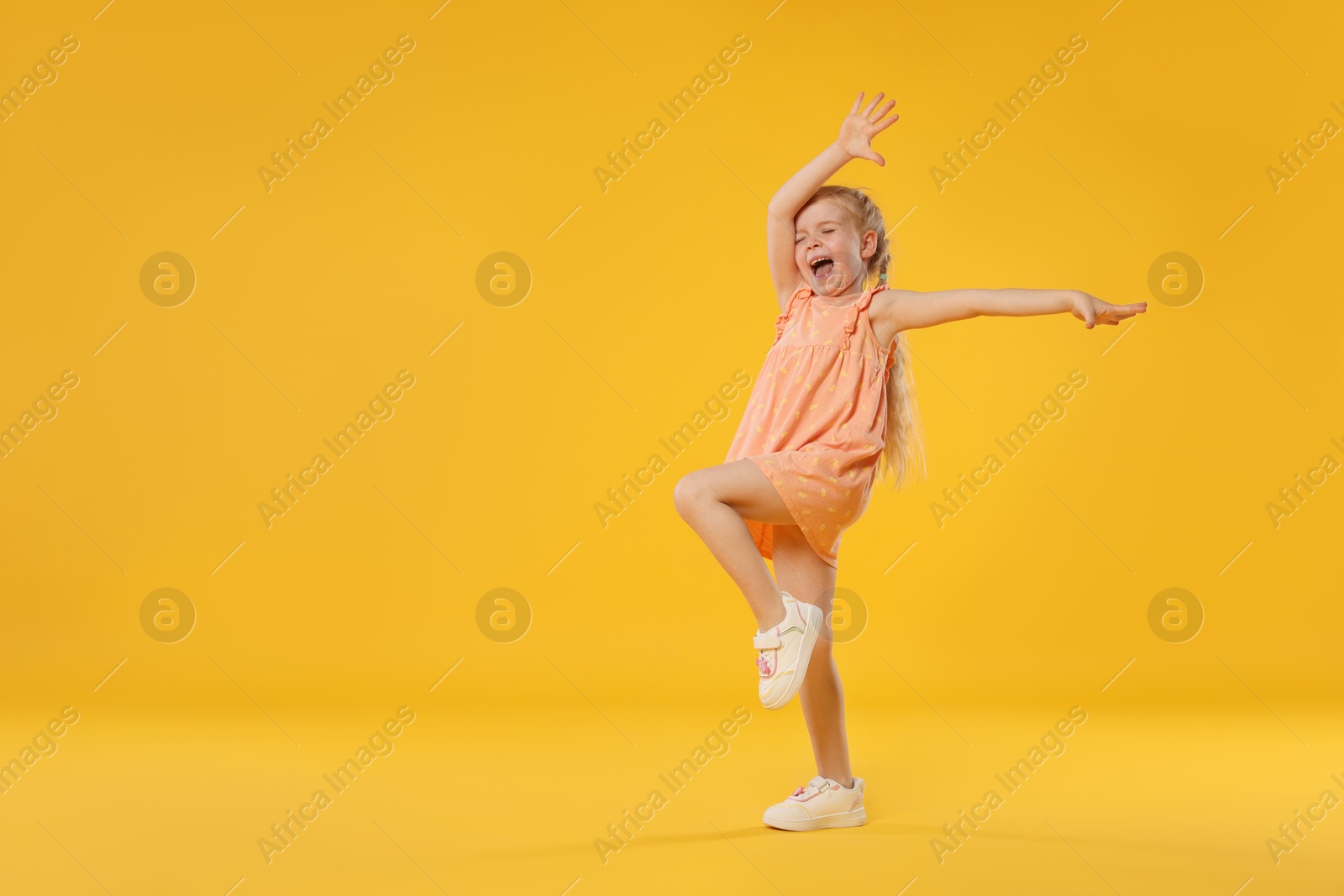 Cute little girl dancing on orange background, space for text Photo of Cute little girl dancing on orange background, space for text