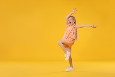 Photo of Cute little girl dancing on orange background, space for text