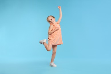 Photo of Cute little girl dancing on light blue background