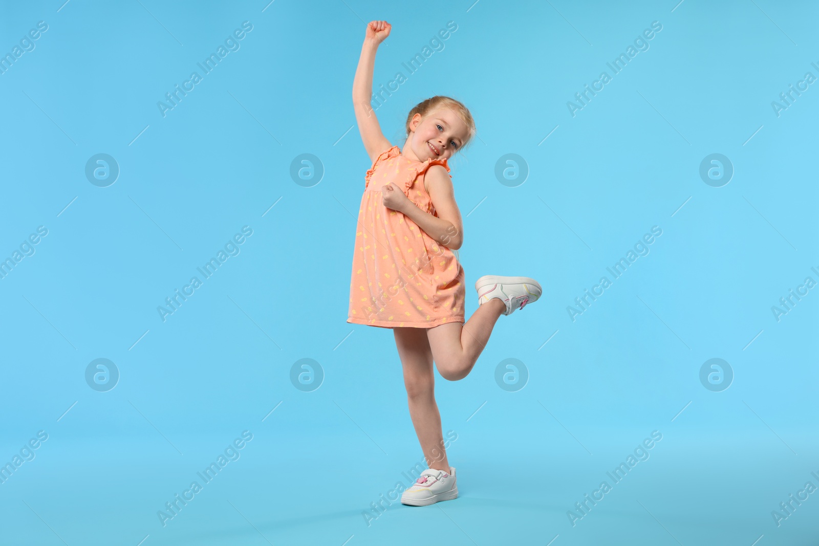 Cute little girl dancing on light blue background Photo of Cute little girl dancing on light blue background