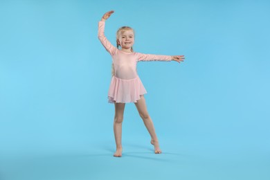Photo of Cute little girl dancing on light blue background