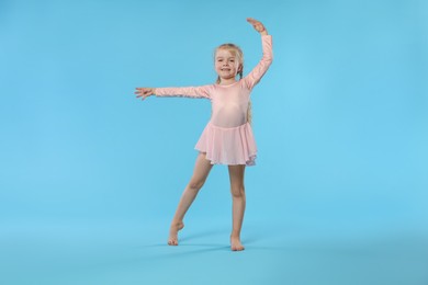 Photo of Cute little girl dancing on light blue background