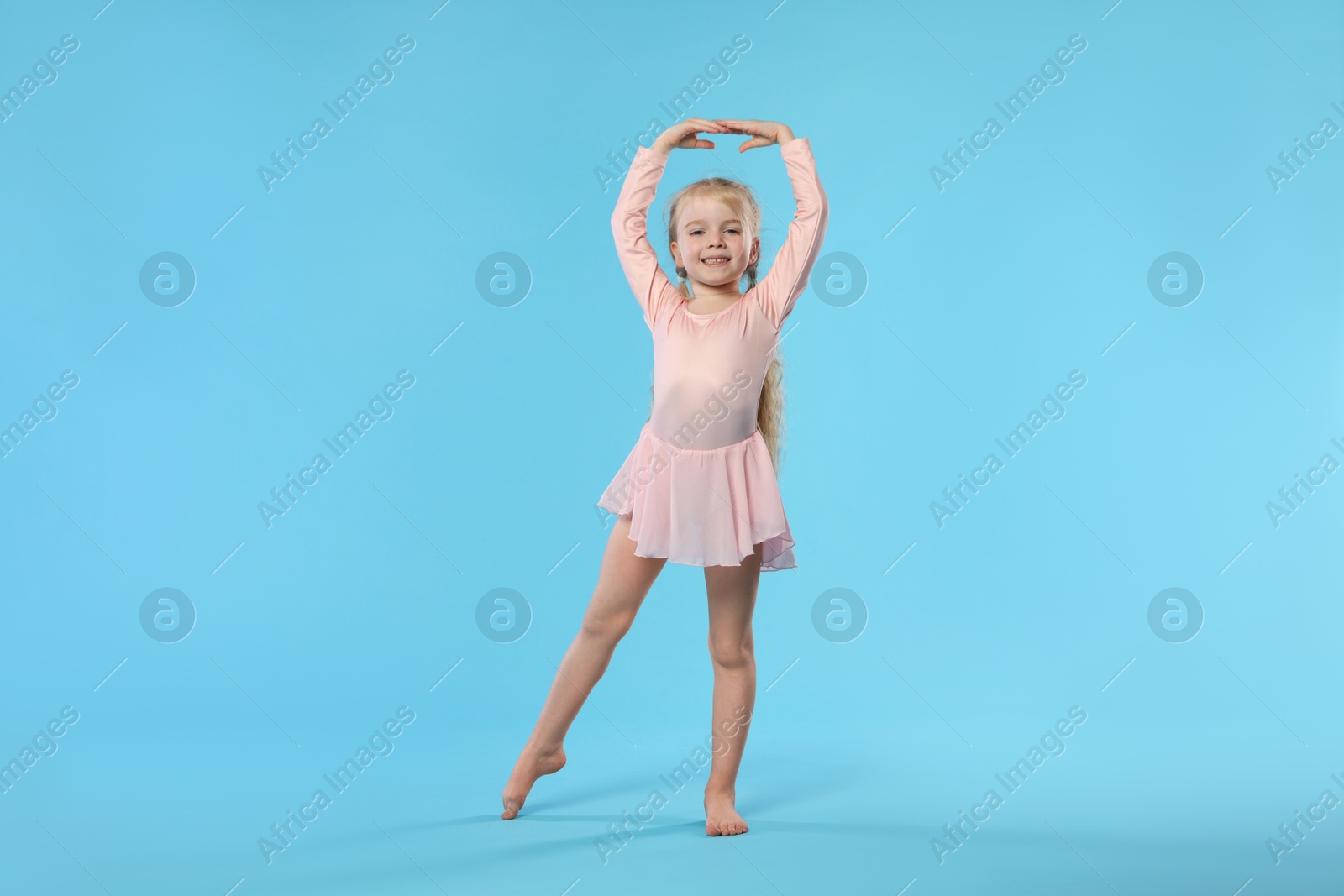 Cute little girl dancing on light blue background Photo of Cute little girl dancing on light blue background