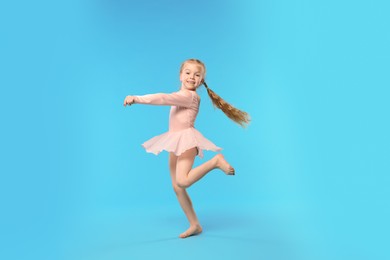 Photo of Cute little girl dancing on light blue background